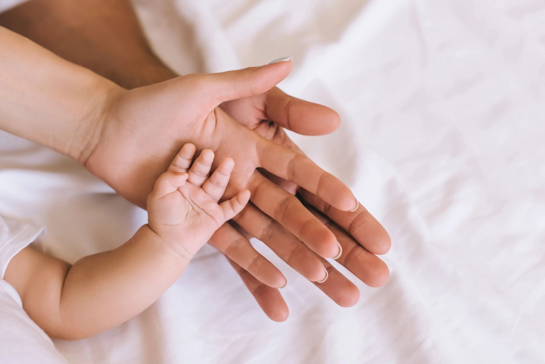 A small baby's hand held securely and gently by two adult hands, illustrating parental care and safety.