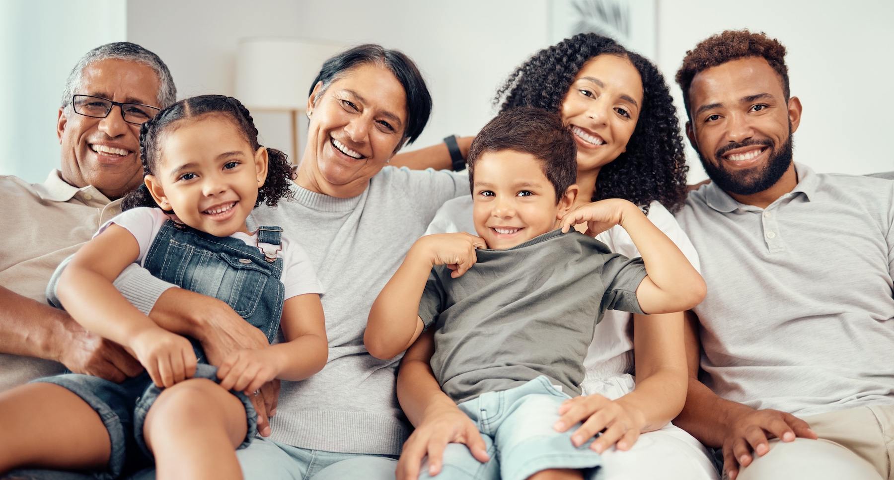 Happy multigenerational family sitting together at home—emphasizing the importance of shared hygiene and safety practices for young children's health.