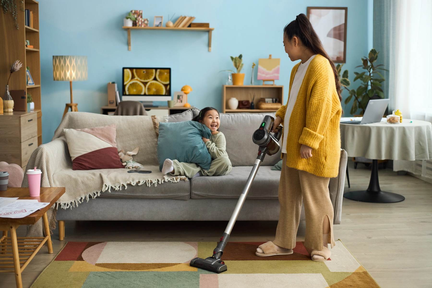 Parent vacuuming living room while child relaxes on couch—routine cleaning improves indoor air quality for healthier homes with young children.
