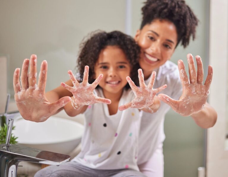 Smiling mother and young daughter displaying soapy hands after proper handwashing for measles prevention in Cayman Islands bathroom