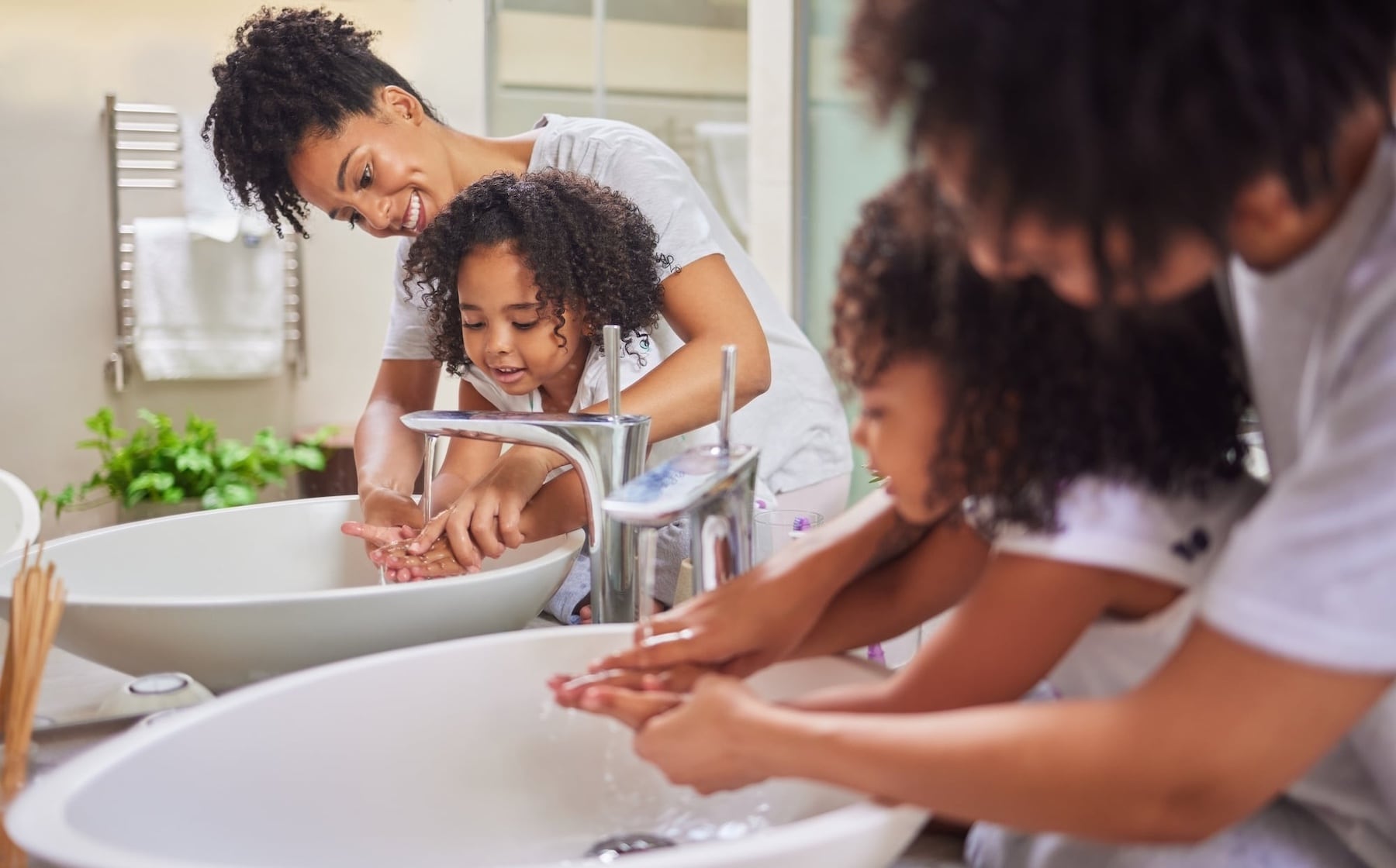 Mother teaching young child proper handwashing technique at bathroom sink for measles prevention in Cayman Islands