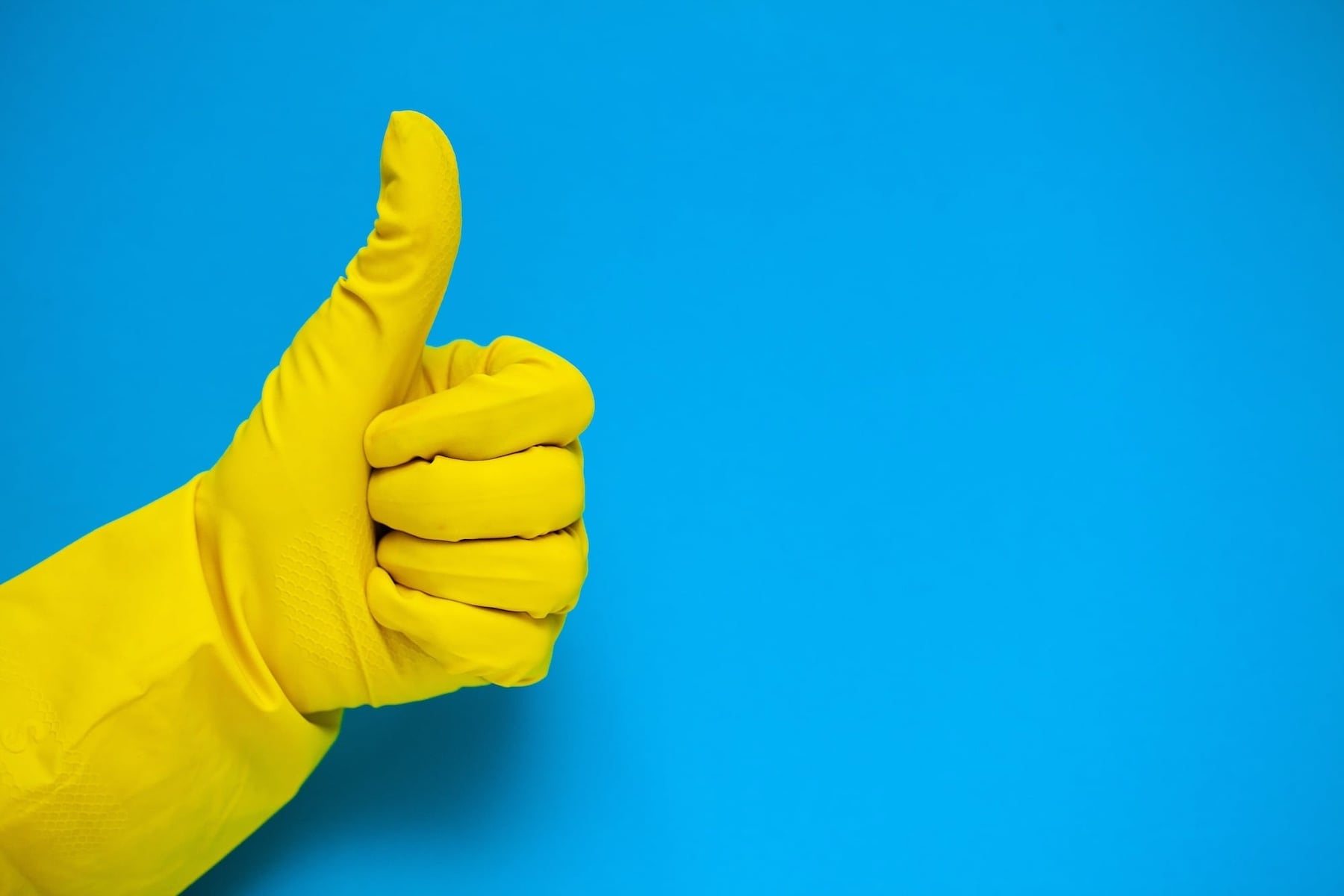 Yellow rubber cleaning glove giving thumbs up gesture against blue background for professional disinfection